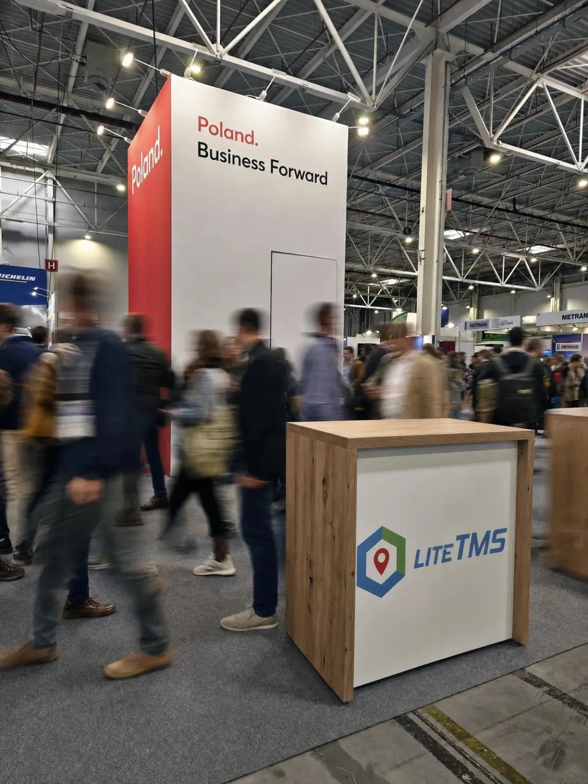 Сапраўдная фатаграфія стойкі LiteTMS і стэнда Poland. Business Forward з фігурамі людзей, дададзенымі штучным інтэлектам з эфектам доўгай вытрымкі